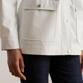 Model wearing Lauren Mascarpone Cream coat, close-up showing patch pockets and silver snap buttons, styled with dark denim jeans.