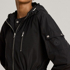 Model wearing Lauren black coat, close-up showing zip-front fastening, chest zip pockets, silver hardware and hooded neckline.