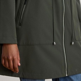 Model wearing Lauren coat in Litchfield Loden, close-up of zip detail, drawstring hem, and side pocket with blue jeans visible.