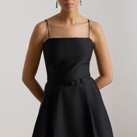 Model wearing Lauren black dress with square neckline, thin straps, and belted bow waist, styled with green drop earrings