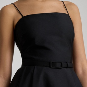 Model wearing Lauren black dress with thin shoulder straps and bow-detail belt at waist, structured bodice, close-up view.