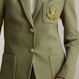 Model wearing Lauren jacket in Light Agave with gold monogram crest badge and embossed gold buttons, single-breasted tailored cut.