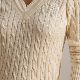 Model wearing Lauren cable-knit V-neck sweater in Mascarpone Cream with embroidered logo detail at chest
