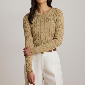 Model wearing Lauren Birch Tan cable-knit jumper with embroidered logo, styled with white wide-leg trousers and brown belt