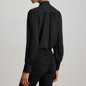 Model wearing Lauren black shirt with gathered yoke detail, long blouson sleeves and buttoned cuffs, styled with dark jeans