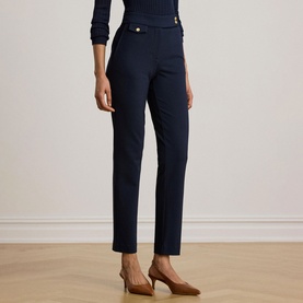 Model wearing Lauren navy slim-leg trousers with gold button detail at waist, styled with a navy top and tan heels.