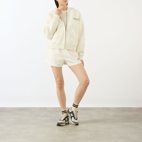 Model wearing Sporty & Rich ecru cotton hoodie with matching shorts and multicolour chunky trainers with white ankle socks.