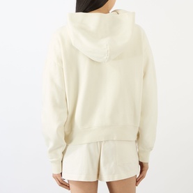 Model wearing Sporty and Rich ecru cotton hoodie, rear view, styled with matching shorts.