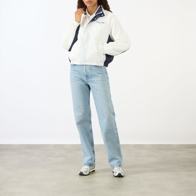 Model wearing Sporty and Rich white and navy zip-up jacket styled with light blue straight-leg jeans and grey trainers.