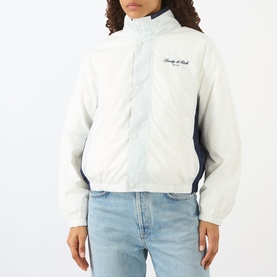 Model wearing Sporty and Rich white and navy zip-up windbreaker jacket with script logo, styled with light blue jeans.