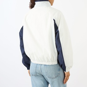 Model wearing Sporty and Rich white and navy colour-block jacket, rear view, styled with light blue jeans.