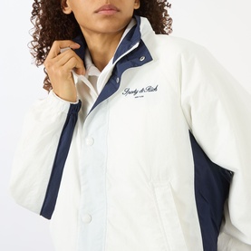 Model wearing Sporty and Rich white and navy jacket with snap button fastening and embroidered logo to chest.