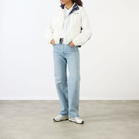 Model wearing Sporty and Rich white and navy jacket, styled with light wash straight-leg jeans and white chunky trainers.