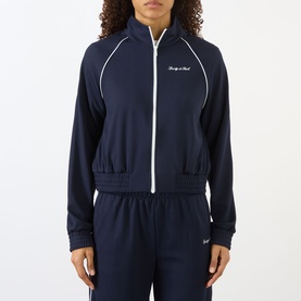 Model wearing Sporty and Rich dark navy zip-up track jacket with white piping and script logo, styled with matching navy track pants.