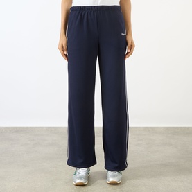 Model wearing Sporty and Rich dark navy wide-leg track pants with white side stripes and elasticated waist, styled with white trainers.