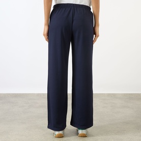 Model wearing Sporty and Rich Dark Navy wide-leg trousers with White waistband detail, rear view, styled with cream shoes.