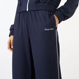 Model wearing Sporty and Rich dark navy wide-leg trousers with white side stripe and embroidered logo, paired with matching jacket