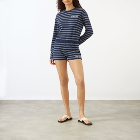 Model wearing Sporty and Rich Dark Navy and White striped shorts, styled with matching long-sleeve top and tan sandals.