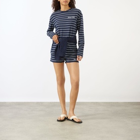 Model wearing Sporty and Rich Dark Navy and White striped shorts with matching long-sleeve stripe top and white sandals.