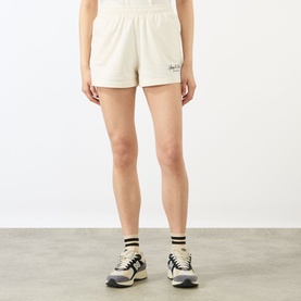 Model wearing Sporty and Rich ecru cotton shorts, styled with striped socks and chunky trainers.