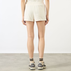 Model wearing Sporty and Rich ecru cotton shorts, rear view, styled with white socks and grey trainers.