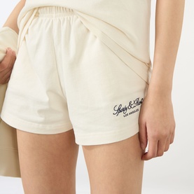 Model wearing Sporty & Rich ecru cotton shorts with navy script logo, styled with matching ecru top