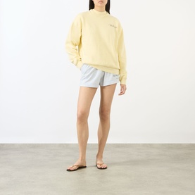 Model wearing Sporty and Rich Almond Navy cotton sweatshirt with light blue shorts and tan sandals