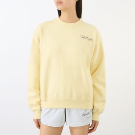 Model wearing Sporty and Rich Almond Navy cotton sweatshirt with cursive chest script, styled with light grey shorts.