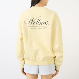 Model wearing Sporty & Rich Wellness sweatshirt in Almond Navy, back view, with light grey shorts.
