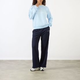 Model wearing Sporty and Rich ciel blue crew neck sweatshirt with navy wide-leg trousers and white trainers