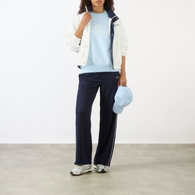 Model wearing Sporty and Rich Ciel sweatpants, styled with a light blue tee, white zip jacket, matching cap and white trainers.