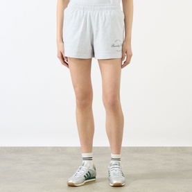 Model wearing Sporty and Rich grey cotton shorts with script logo, styled with white socks and green trainers.