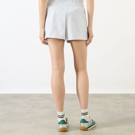 Model wearing Sporty and Rich grey cotton shorts, shown from behind, styled with white socks and green trainers.
