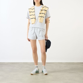 Model wearing Sporty and Rich grey cotton shorts with a yellow striped vest, white tee, green trainers and navy cap.
