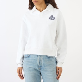 Model wearing Sporty and Rich white cropped polo-collar sweatshirt with navy crest embroidery, styled with light blue jeans.