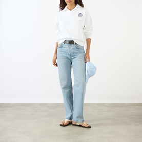 Model wearing Sporty and Rich white sweatshirt with light wash straight-leg jeans, blue cap and brown sandals