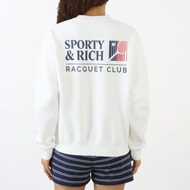 Model wearing Sporty and Rich white Racquet Club sweatshirt, back view, styled with navy striped shorts.