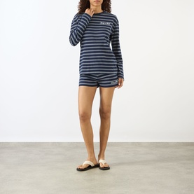 Model wearing Sporty and Rich Dark Navy and White striped long-sleeve T-shirt, styled with matching shorts and brown sandals.