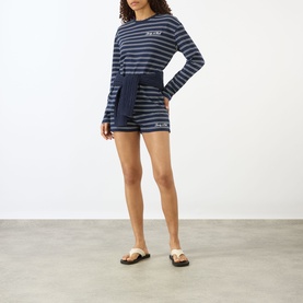 Model wearing Sporty and Rich dark navy and white striped long-sleeve T-shirt, styled with matching striped shorts and tan sandals.