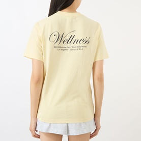 Model wearing Sporty and Rich Almond Navy Wellness T-shirt, back view, paired with light grey shorts