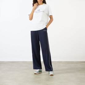 Model wearing Sporty and Rich white graphic T-shirt, styled with navy wide-leg track pants and silver trainers.