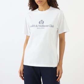 Model wearing Sporty and Rich Health & Wellness Club white crew-neck T-shirt, styled with navy trousers