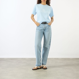 Model wearing Sporty and Rich Ciel T-shirt with light wash straight-leg jeans, black belt and brown leather sandals.