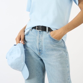 Model wearing Sporty and Rich Ciel T-shirt with light wash wide-leg jeans and black belt, holding a pale blue cap