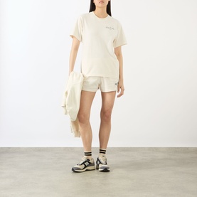 Model wearing Sporty & Rich ecru oversized cotton T-shirt with matching shorts and chunky trainers, holding a cream jacket.