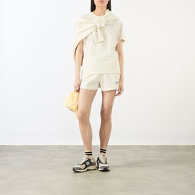 Model wearing Sporty and Rich ecru cotton T-shirt with oversized bow detail, styled with matching shorts and chunky trainers.