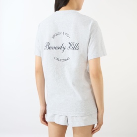 Model wearing Sporty and Rich Heather Grey Beverly Hills cotton T-shirt, back view, styled with matching grey shorts.