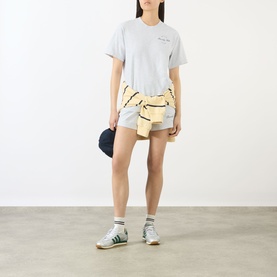 Model wearing Sporty and Rich Heather Grey cotton T-shirt with mini shorts, yellow tied shirt and green trainers.
