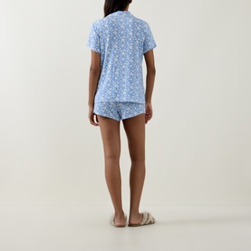 Model wearing Stripe & Stare La Jardin Bleu pyjama short set, blue floral print short-sleeve shirt and shorts, styled with cream slippers.
