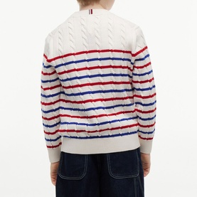 Model wearing white cable-knit sweater with red and blue horizontal stripes, shown from the back, styled with navy trousers